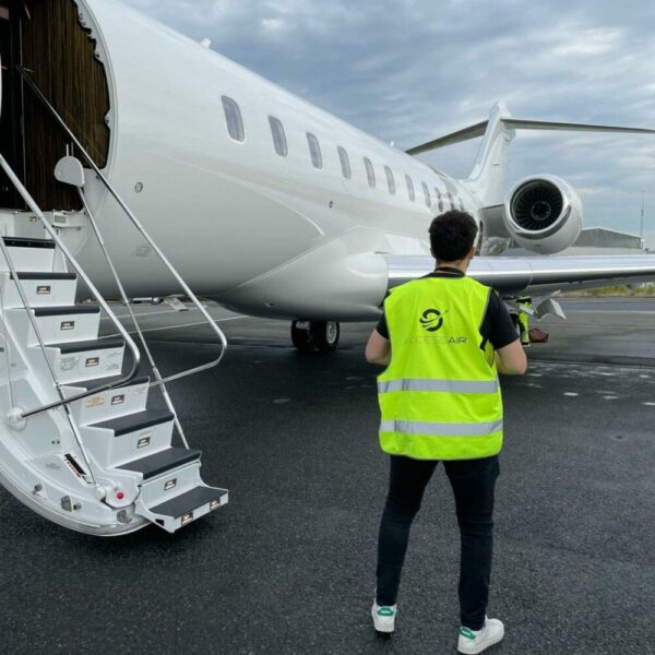 Un homme avec un gilet jaune accessair se tient de dos en face d'un jet privé stationné à l'aéroport